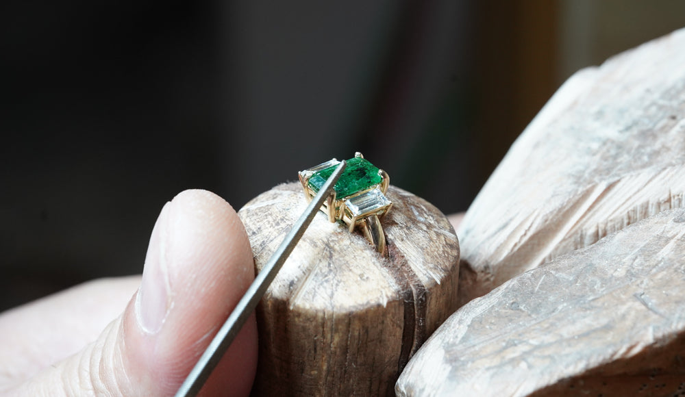 A goldsmith setting an emerald and diamond ring at the bench