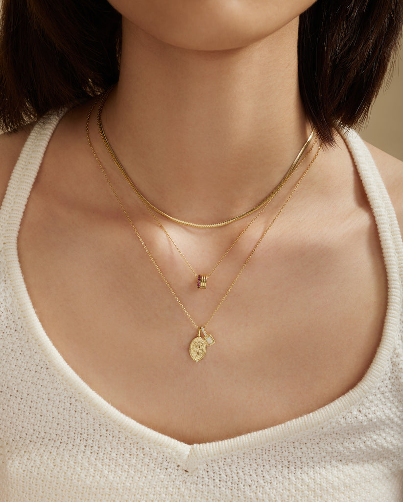 Close-up of a person wearing two gold necklaces with pendants on a neutral background