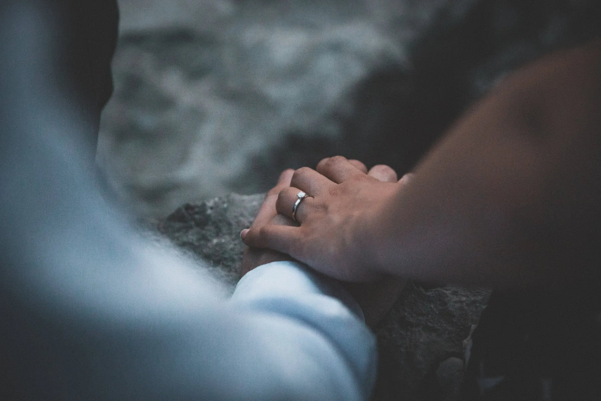 Couple holding hands outdoors, a solitaire diamond engagement ring on her finger
